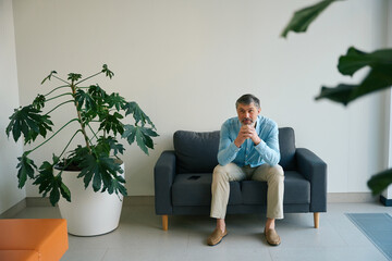 Portrait of man sitting on couch surrounded houseplant in hospital