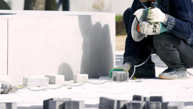 Man city worker measures and cuts paving slab with grinding machine in city park. Male wears regular clothes and gloves crop body slow motion