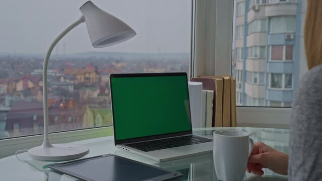 businesswoman has a break at workspace with view of cityscape laptop with green screen on the desk in apartment businesswoman working online