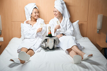 Two ladies in bathrobes drink champagne in a hotel room