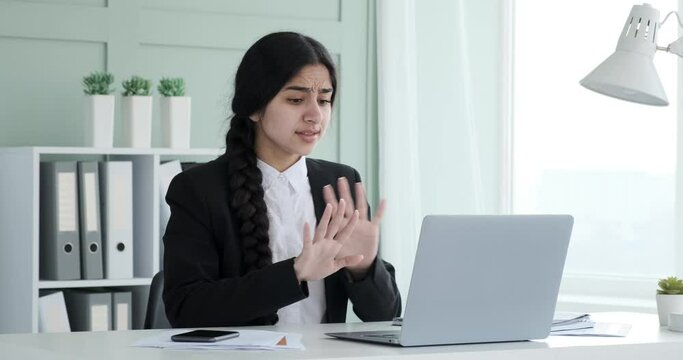 Indian businesswoman sits in office working on laptop. She made an irreversible mistake. Frantically pressing buttons on laptop, she tries to undo the action. She anxiously clasp her hand to head.