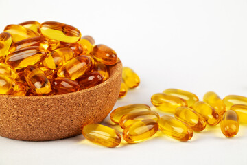 Cod liver oil omega 3 gel capsules in bowl on white background.