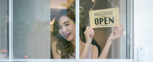 Woman store owner turning open sign broad through the door glass and ready to service. Small...
