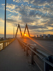 Obraz premium Orange sunset over the bridge over the river in the city. World Sun Day. Bridge Day