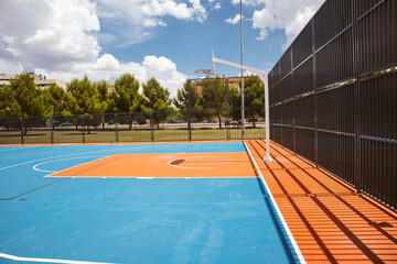 Empty outdoor basketball court in the garden and blue sky. Blue red basketball court for soccer,...