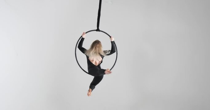 Confident Caucasian dancer as she showcases her acrobatic prowess on the aerial hoop. With a striking black jumpsuit and barefoot, she effortlessly moves through the air.