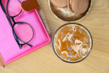 Iced latte coffee in glass on cafe table with notebook. Summer cold coffe drink and business time