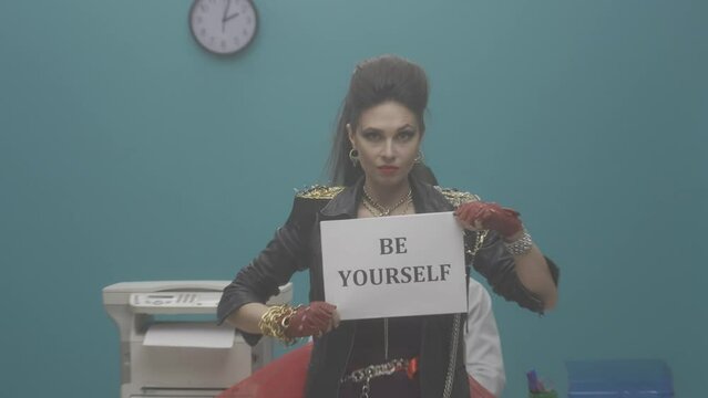 The female freak holds a sheet of paper with words BE YOURSELF and then scatters them. Woman in a black leather jacket with chains in the office. Advertising. Slow motion. HDR BT2020 HLG Material