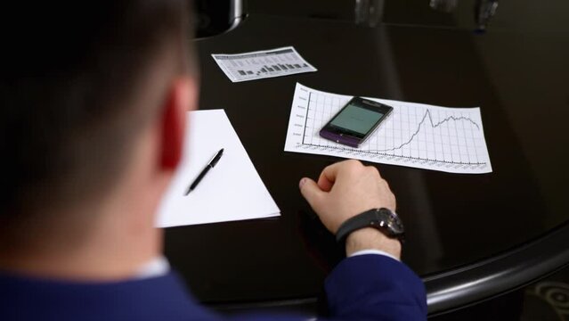 Manager ringing mobile phone on black office table at meeting on blurred background. Man wants take cell phone crop body back view