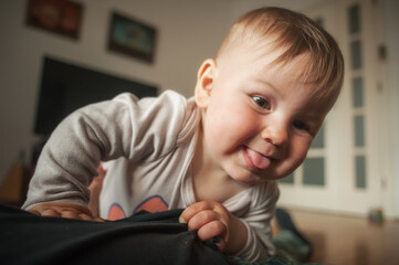 Fototapeta premium Close-up portrait of cute funny and joyful smiling baby boy, stuck out its tongue. Joy and happiness concept. Love and family emotion