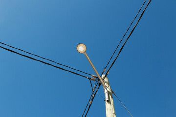 Street light in a wooden post with crossed cables and sky background..