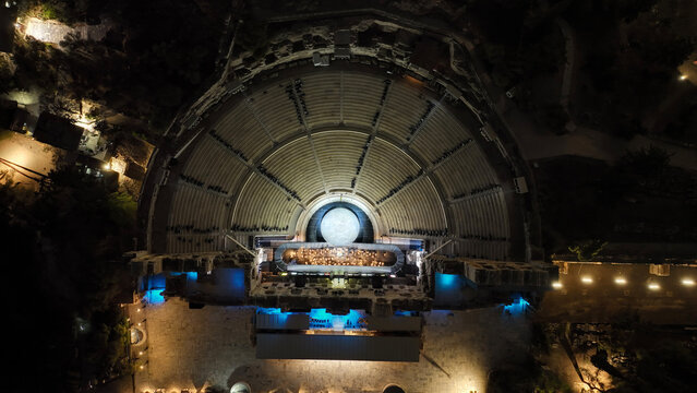 Aerial drone night shot of iconic illuminated ancient amphitheatre of Herodes Atticus built in the slopes of Acropolis hill, Athens, Attica, Greece