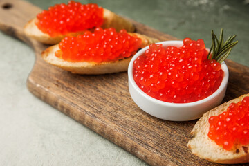 Tasty bruschettas with red caviar on color background