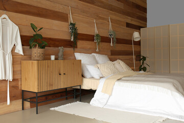 Interior of bedroom with wooden cabinet, cozy bed and hanging houseplants