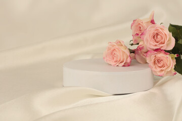 Pink rose flower bouquet on white podium and silk fabric.. Light beige background. Minimal empty display product presentation scene.