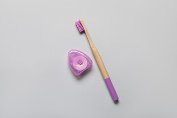 Dental floss and purple bamboo toothbrush on grey background