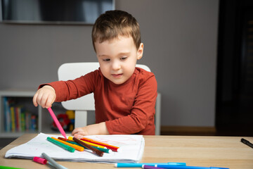 A cute happy little toddler boy of two years old draws with markers in the album in the children's room at home. Educational activities for kids. Selective focus
