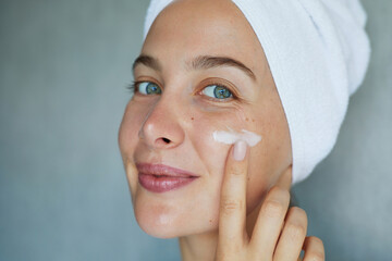 Morning skin care routine. Young beautiful woman is applying  a cream, scrub beauty product on her...