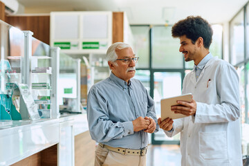 Obraz premium Senior man and young pharmacist using digital tablet in pharmacy.