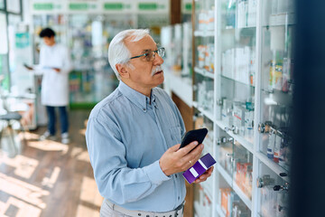 Senior man using cell phone while looking for medicine in pharmacy.