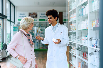 Happy Muslim pharmacist talks to senior woman in drugstore.