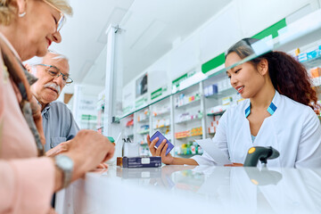 Happy Chinese pharmacist assists her senior customers in buying medicine in pharmacy.