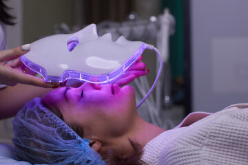 LED light anti-aging mask for facial skin care in a spa slow motion. A woman lies on a couch in a special mask. Modern technologies of beauty and health. - obrazy, fototapety, plakaty