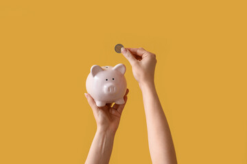 Woman with coin and piggy bank on yellow background