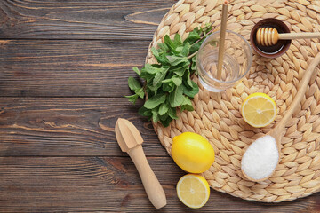 Wicker mat with glass, lemons and mint on brown wooden background