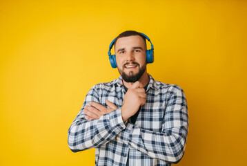 Photo of a handsome guy listening to youth music in his ears, dancing a young man in a plaid shirt and trousers on a yellow background