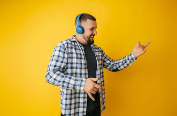 Photo of a handsome guy listening to youth music in his ears, dancing a young man in a plaid shirt and trousers on a yellow background