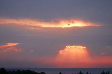 Picturesque summer landscape. Sunset over the river. The rays of the setting sun are breaking through a gap in the clouds. Selective Focus.