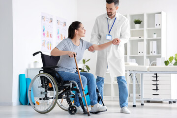 Male physiotherapist helping young woman to stand up in rehabilitation center - Powered by Adobe