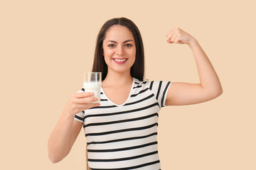 Fototapeta premium Healthy young woman with glass of milk on beige background