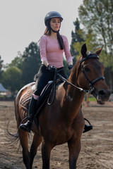 Close up on a young woman wearing a helmet who is riding a horse in an equestrian center