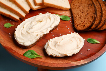 Wooden stand of tasty sandwiches with cream cheese on blue background