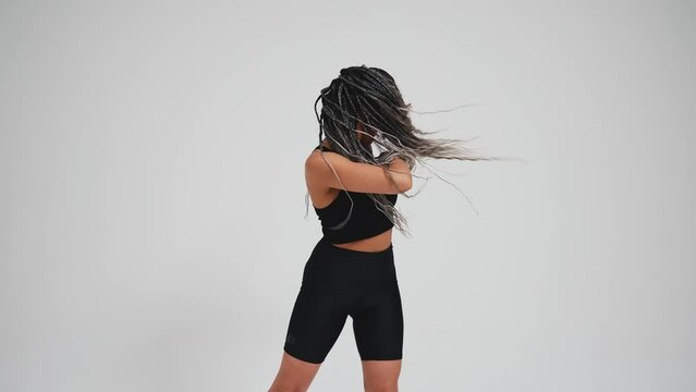African pretty woman with pigtails in black tracksuit dancing against gray background in studio