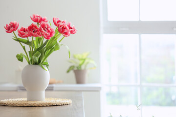 Vase with tulips on table in light kitchen