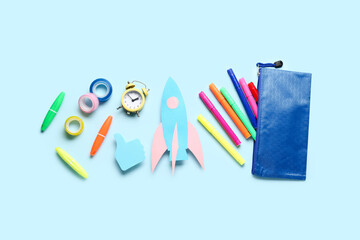 Paper rocket with pencil case and different stationery on blue background