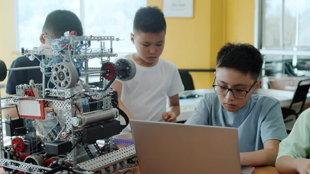 Children in a class at a robotics lesson assemble modules for the moving robot and use the laptop for programming it. Concept of technological modern education