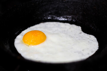 A perfectly fried egg sizzling in a black cast iron frying pan, accentuated by the dark backdrop of night. The golden yolk and crispy edges of the egg create an appetizing sight. Out of focus