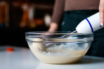 A skilled chef's hand prepares homemade mayonnaise by beating together ingredients in a glass bowl. chef uses a blender to mix the creamy sauce, adding olive oil for a rich and smooth texture