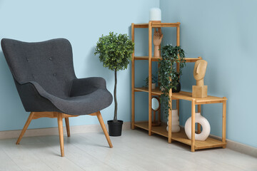 Dark grey armchair with shelving unit, houseplants and sculptures near blue wall