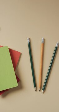 Vertical video of overhead view of school stationery on beige background, in slow motion
