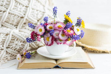 Congratulations for Mother's or Women's day, birthday or anniversary. Countryside decor, old book, wooden background, straw hat. Greeting postcard with bright summer or spring flowers in a cute cup