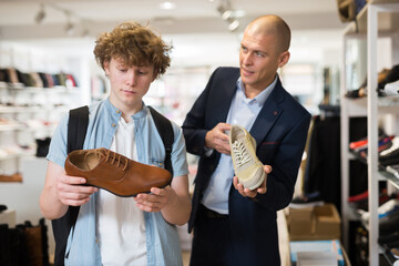 Man wearing in suit and teenager looking for comfortable classic shoes in shoe store.