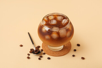 Glass of ice coffee with beans and spoon on beige background