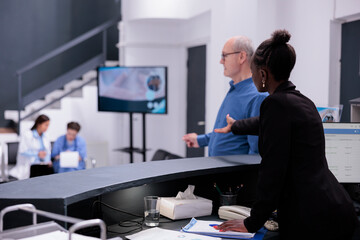 Reception worker telling sick old man to take a seat in waiting area during checkup visit appointment in hospital. Elderly man having medical consultation with physician doctor, health care service