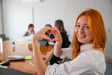 Smiling businesswoman makes heart with hands in office, person who loves her job