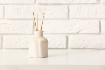 Bottle of reed diffuser on table near light brick wall in room
